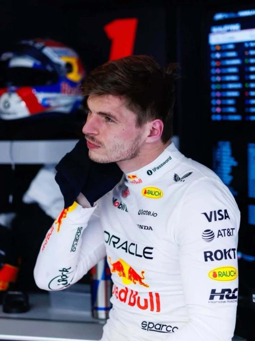 Person in a racing suit with various sponsor logos in a garage setting