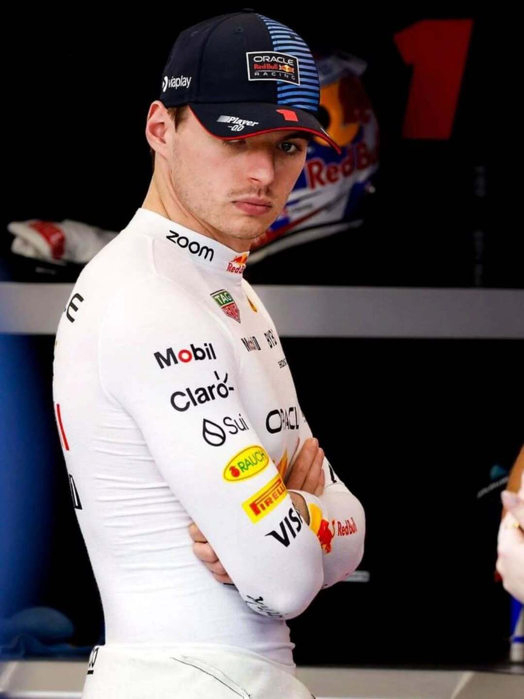 Person wearing a racing suit with various sponsor logos in a garage setting