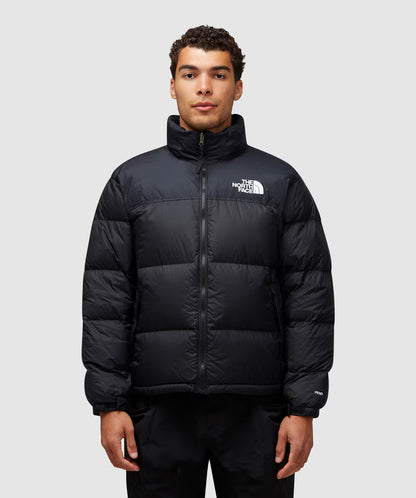 Person wearing a black puffer jacket with The North Face logo on a light gray background