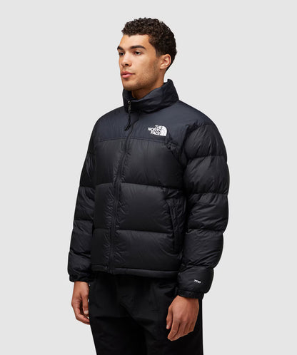 Person wearing a black puffer jacket with a brand logo on a light gray background