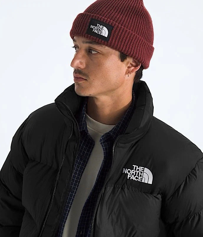 Person wearing a red beanie and black The North Face jacket on a white background