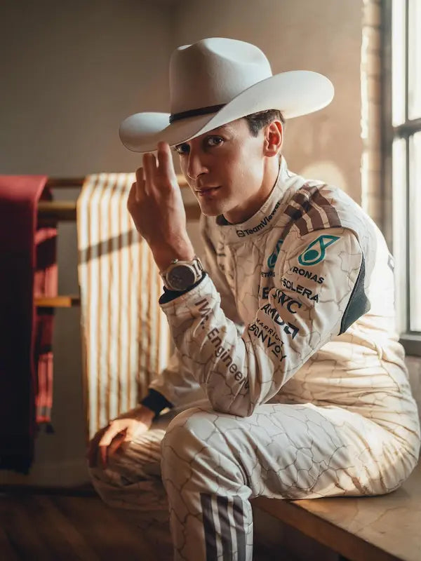 Person wearing a white racing suit with sponsor logos and a cowboy hat indoors.